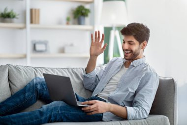 Uzaktan iletişim konsepti. Heyecanlı bir Arap videosu dizüstü bilgisayardan arıyor, kanepede yatıyor, boş yer var.