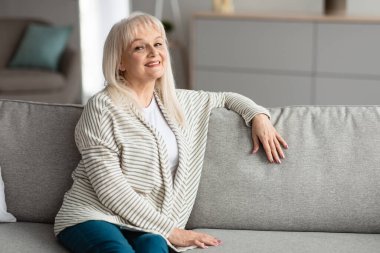 Olgun bir kadın evinde dinleniyor, kameraya bakıyor.