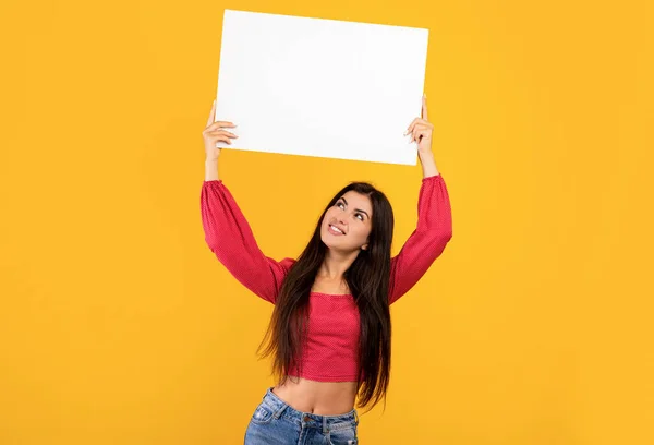 Концепція реклами. Щаслива вірменка тримає порожню порожню дошку і дивиться на жовтий студійний фон — стокове фото