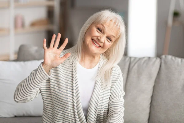 Donna anziana che saluta la macchina fotografica e sorride, seduta sul divano — Foto Stock