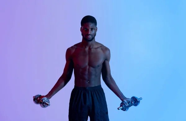 Porträt eines hübschen schwarzen Bodybuilders mit nackter Brust, der mit Hanteln trainiert und Eisen in Neonlicht pumpt — Stockfoto