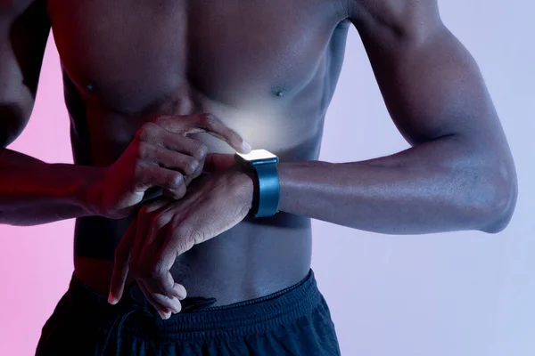 Irreconhecível jovem preto cara com muscular nu torso verificando seu rastreador de fitness no neon luz — Fotografia de Stock
