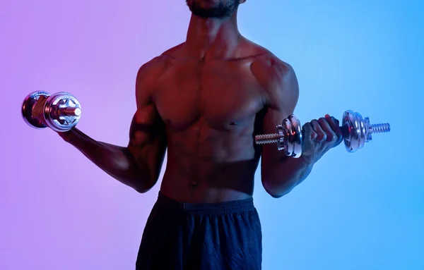 Chico negro irreconocible con entrenamiento corporal sexy con mancuernas, bombeando músculos en luz de neón, primer plano —  Fotos de Stock