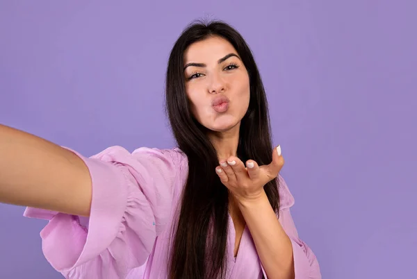 Coquette femme arménienne prendre selfie, souffler baiser d'air sur fond violet studio, faire des photos d'elle-même — Photo