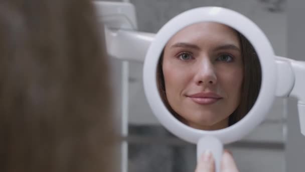 Primer plano retrato de la joven dama alegre mirando al espejo y sonriendo, disfrutando de los dientes blanqueamiento resultado en la clínica dental — Vídeo de stock