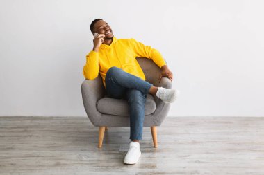 Gülümseyen Afrikalı Erkek Gri Duvar 'ın yanında oturan Cep Telefonuyla Konuşuyor