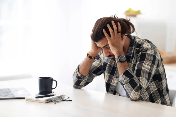 Uomo arabo depresso seduto al tavolo da lavoro, toccandosi la testa — Foto Stock