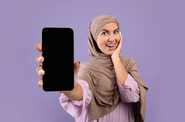 Gambar mockup smartphone dengan layar hitam kosong di tangan wanita muslim yang bahagia berhijab di atas latar belakang ungu — Stok Foto
