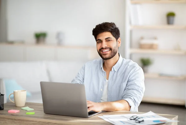Ελεύθερος επαγγελματίας της χιλιετίας. Πορτρέτο του ευτυχισμένου Άραβα άνθρωπος κάθεται στο γραφείο με φορητό υπολογιστή, εργασίας στο γραφείο στο σπίτι, αντίγραφο χώρου — Φωτογραφία Αρχείου