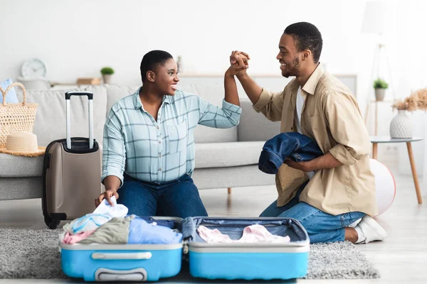 Radosna afroamerykańska para Pakowanie walizki Trzymając się za ręce w domu — Zdjęcie stockowe