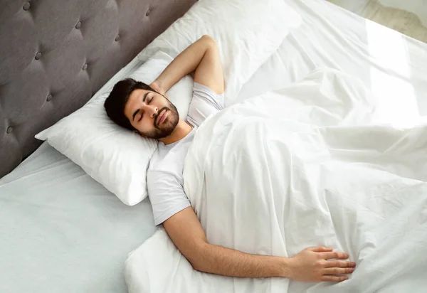 Chico árabe durmiendo descansando tranquilamente en su cómoda cama en casa, acostado con los ojos cerrados, por encima de la vista — Foto de Stock