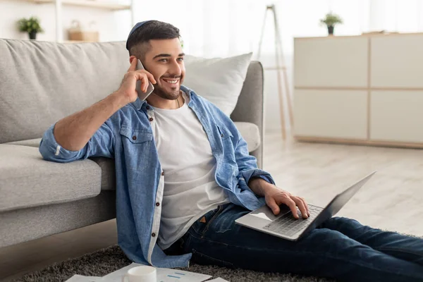 Adam bilgisayarda çalışıyor ve evde cep telefonuyla konuşuyor.