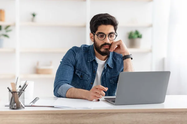 Fiatal arab alkalmazott dolgozik laptop íróasztal otthoni irodában, nézi a számítógép képernyőjén, másolja a helyet — Stock Fotó