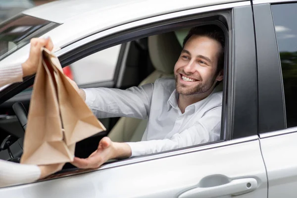 O correio de entrega de comida dá sacos de papel ao homem no carro. Segurança alimentar entregue — Fotografia de Stock