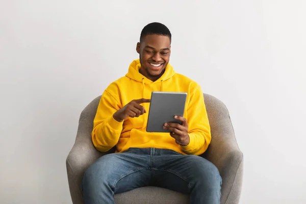 Hombre afroamericano usando tableta digital sentado sobre fondo gris —  Fotos de Stock