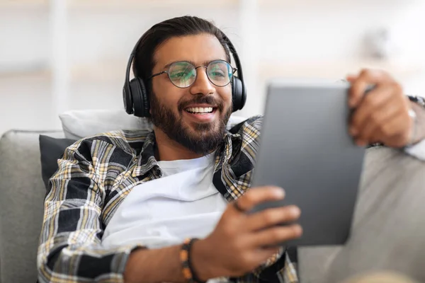 Alegre árabe cara assistindo vídeos no digital tablet em casa — Fotografia de Stock