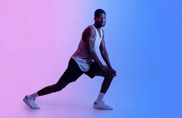 Comprimento total de homem negro desportivo fazendo lunges ou esticando as pernas em luz de néon. Conceito de estilo de vida ativo — Fotografia de Stock