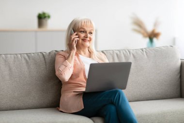 Gülümseyen olgun bir kadın cep telefonuyla çalışıyor ve konuşuyor.