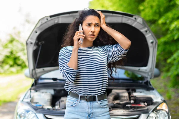 Nervous woman with open car hood calling auto service