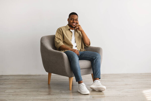 Successful African American Man Posing Sitting In Chair, Gray Background