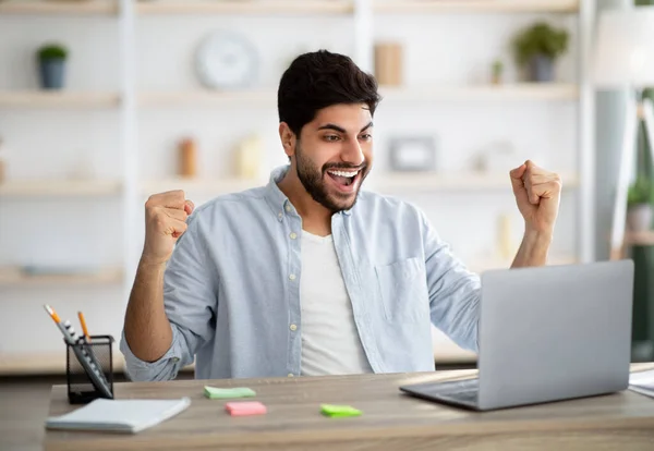 Noticias de promoción. Hombre árabe excitado mirando a la computadora portátil y celebrando su éxito, levantando puños y exclamando con alegría — Foto de Stock