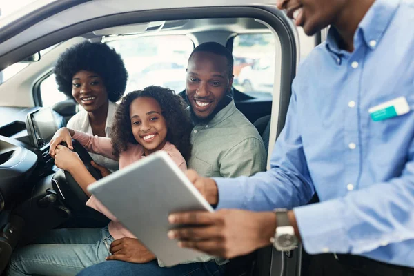 Família negra testando carro novo, vendedor mostrando-lhes compra ou contrato de locação em tablet digital na concessionária de automóveis — Fotografia de Stock