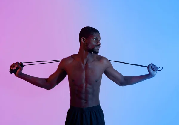 Retrato de deportista negro determinado con cuerpo musculoso sosteniendo saltar la cuerda en la iluminación de neón —  Fotos de Stock