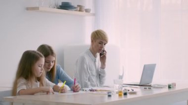 Çevrimiçi çalışan iki kızın annesi içeride telefonla konuşuyor.