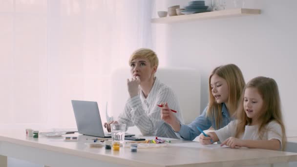 未就職の母がノートパソコンで座りながら、娘たちが屋内を描く — ストック動画