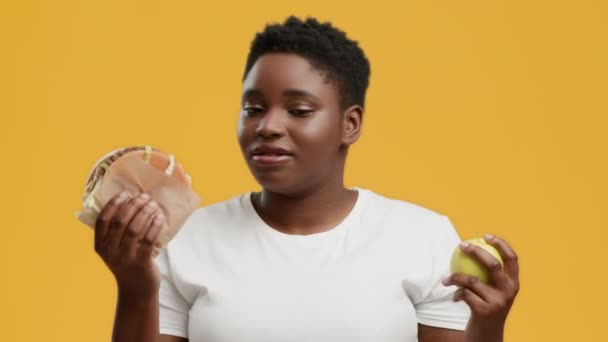 Elhízott afrikai hölgy kiválasztása alma helyett Burger, sárga háttér — Stock videók