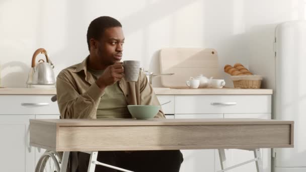 Στοχαστικό άτομα με ειδικές ανάγκες μαύρο άνδρα σε αναπηρική καρέκλα έχοντας πρωινό στην κουζίνα — Αρχείο Βίντεο