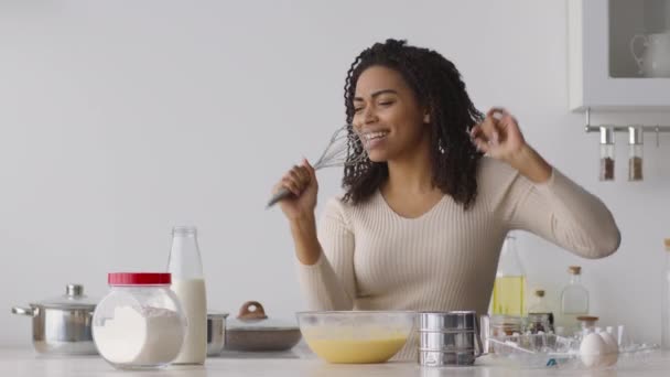 若い正のアフリカ系アメリカ人の女性は、パン屋のための生地を調理しながら、台所で泡立て器とダンスに歌う — ストック動画