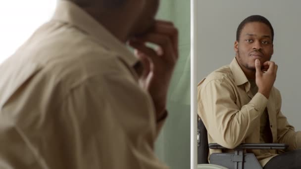 Afrikansk kille i rullstol tittar på reflektion i spegeln inomhus — Stockvideo