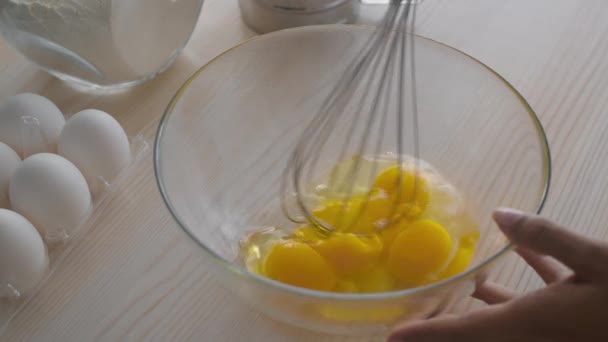 Perinteinen aamiainen resepti. Musta nainen vispilä munia lasikulhossa keittiössä, ruoanlaitto munakokkelia perheelle, hidastettuna — kuvapankkivideo