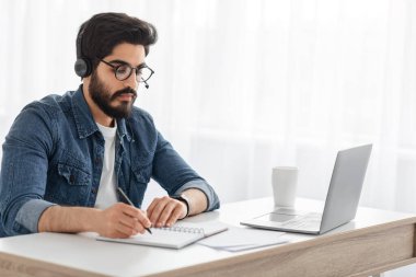 Modern eğitim. Arap öğrenci evde öğreniyor, dizüstü bilgisayara bakıyor, masada oturuyor, boş yer var.