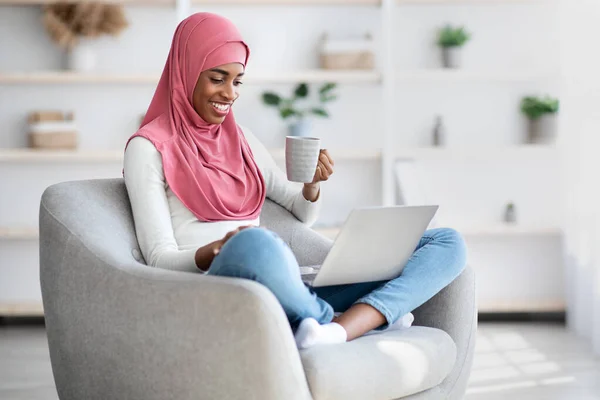 Feliz negro musulmán mujer relajarse con el ordenador portátil y beber café en casa — Foto de Stock