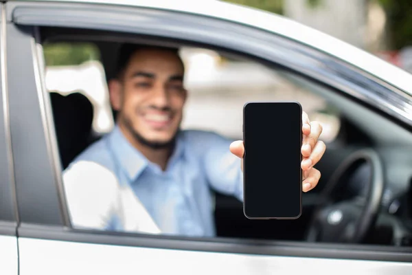 Vidám arab férfi ül az autóban, mutatja a mobilját, mockup — Stock Fotó
