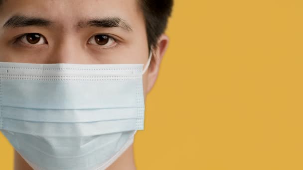 Koreansk man bär skyddande ansiktsmask över gul bakgrund, beskuren — Stockvideo