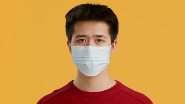 Serieuze aziatische man dragen beschermende gezicht masker over gele achtergrond — Stockvideo