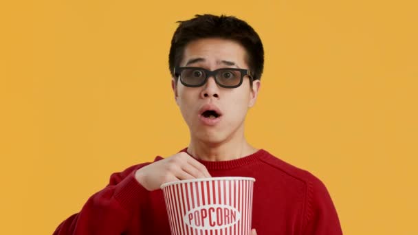 Chockad kinesisk man bär 3D-glasögon äta popcorn, gul bakgrund — Stockvideo