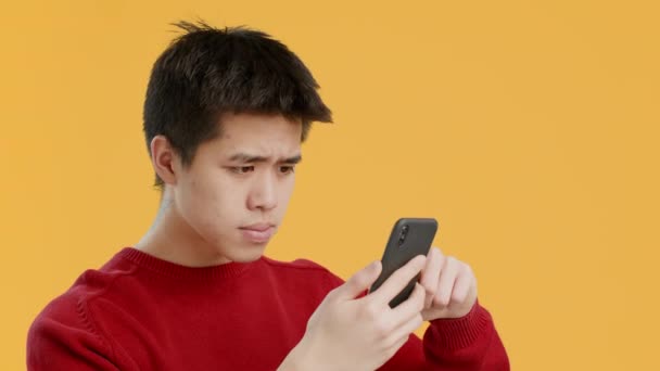 Japonés hombre usando teléfono desplazamiento y cabeza de asentimiento, fondo amarillo — Vídeos de Stock