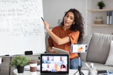 Matematik öğretmeni beyaz tahtayı gösteriyor, öğrencilere çevrimiçi ders veriyor