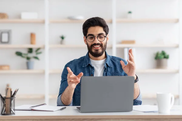 Tutorat en ligne. Amical arabe gars ayant une vidéoconférence via ordinateur portable, parler à la caméra, assis dans le bureau à la maison — Photo