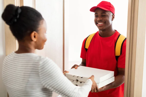 Fröhlicher schwarzer Kurier steht mit Pizzakartons vor der Tür — Stockfoto