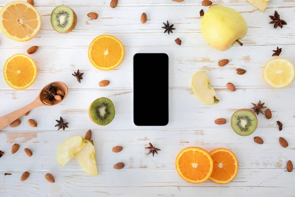 Healthy eating concept. Smartphone with blank black screen on wooden table with fruit slices, almond and star anise, top view — Stock Photo, Image