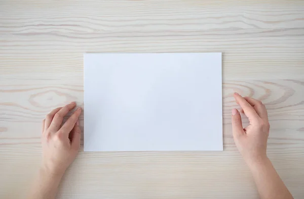 女性手，白色空白纸片，木制桌子背景，顶视图，空空间，平铺 — 图库照片