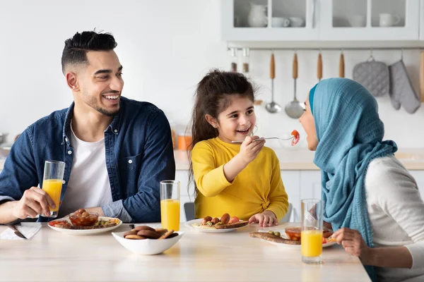 Anne ve babasıyla mutfakta kahvaltı ederken annesini besleyen küçük bir Arap kızı. — Stok fotoğraf