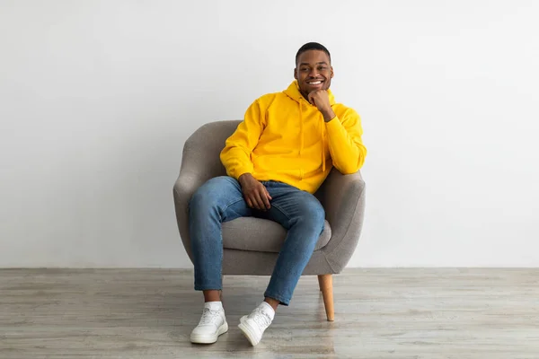 Exitoso negro millennial chico sentado en sillón cerca gris pared — Foto de Stock