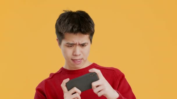 Homem chinês usando telefone jogar jogo on-line sobre fundo amarelo — Vídeo de Stock