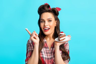 Eski moda kıyafetli seksi genç bayan lezzetli pastalar yiyor, parmağında krema var, mavi stüdyo geçmişi var.